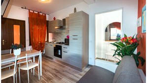 A modern kitchen with white cabinets, a dining area with a table and chairs, and a living room with a sofa and a plant. - Appartamenti Krystall (San Michele al Tagliamento)