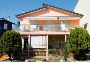 Una casa a due piani con un balcone, un portico coperto e un giardino.