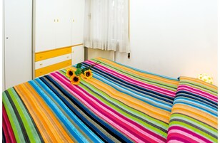 Una stanza con un letto con copriletto a righe colorate, un armadio con dettagli gialli e una finestra con tende bianche.
