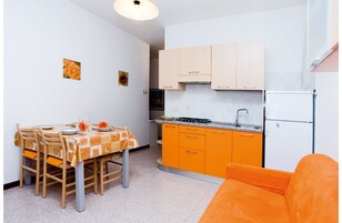 Una cucina compatta con zona pranzo, che include un tavolo apparecchiato per due, un divano e un piccolo divanetto arancione.