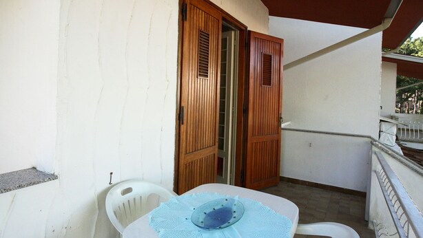 Ein kleiner Balkon mit weißem Tisch und Stühlen, einer Holztür und einer weißen Wand.