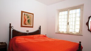 Ein Schlafzimmer mit einem hölzernen Bett, einem Nachttisch, einem Fenster mit Vorhängen und einem gerahmten Bild an der Wand.