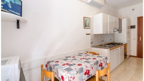 Una cocina compacta con armarios blancos, una pequeña mesa de comedor con mantel floral y un televisor montado en la pared.