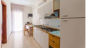 Una cocina con gabinetes blancos, estufa a gas, lavamanos y microondas.