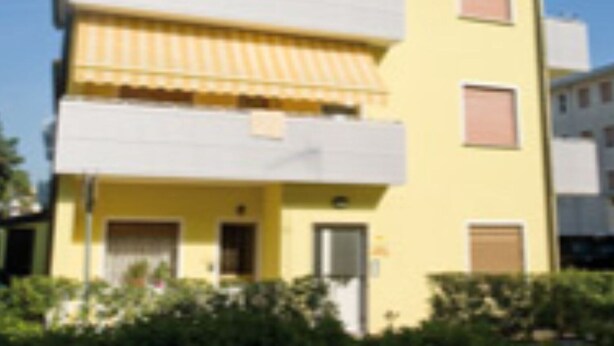 Un immeuble à plusieurs étages, doté d’une façade jaune, de balcons et d’une antenne visible.