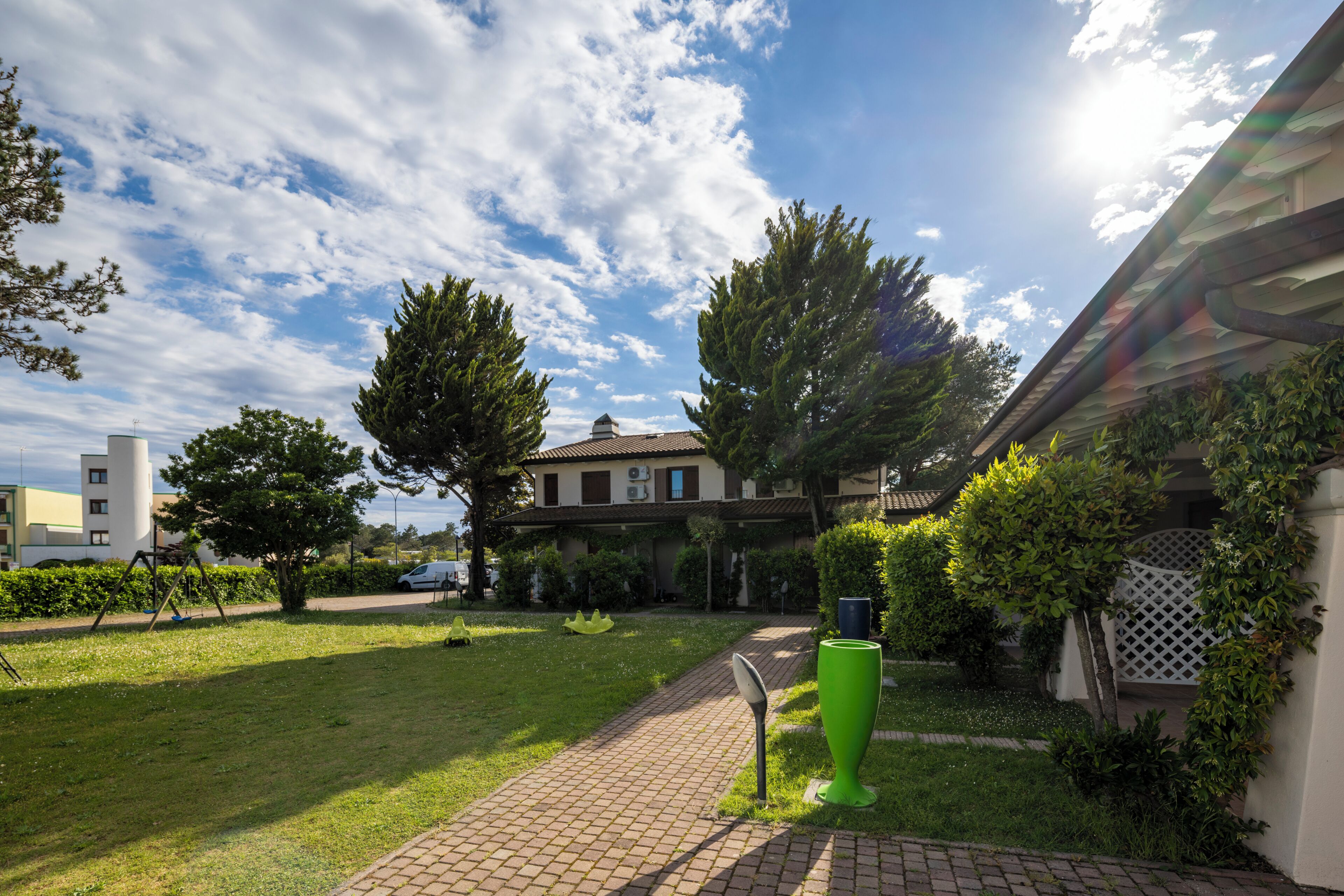 A residential area with a paved pathway, a green planter, and a house with a tiled roof.