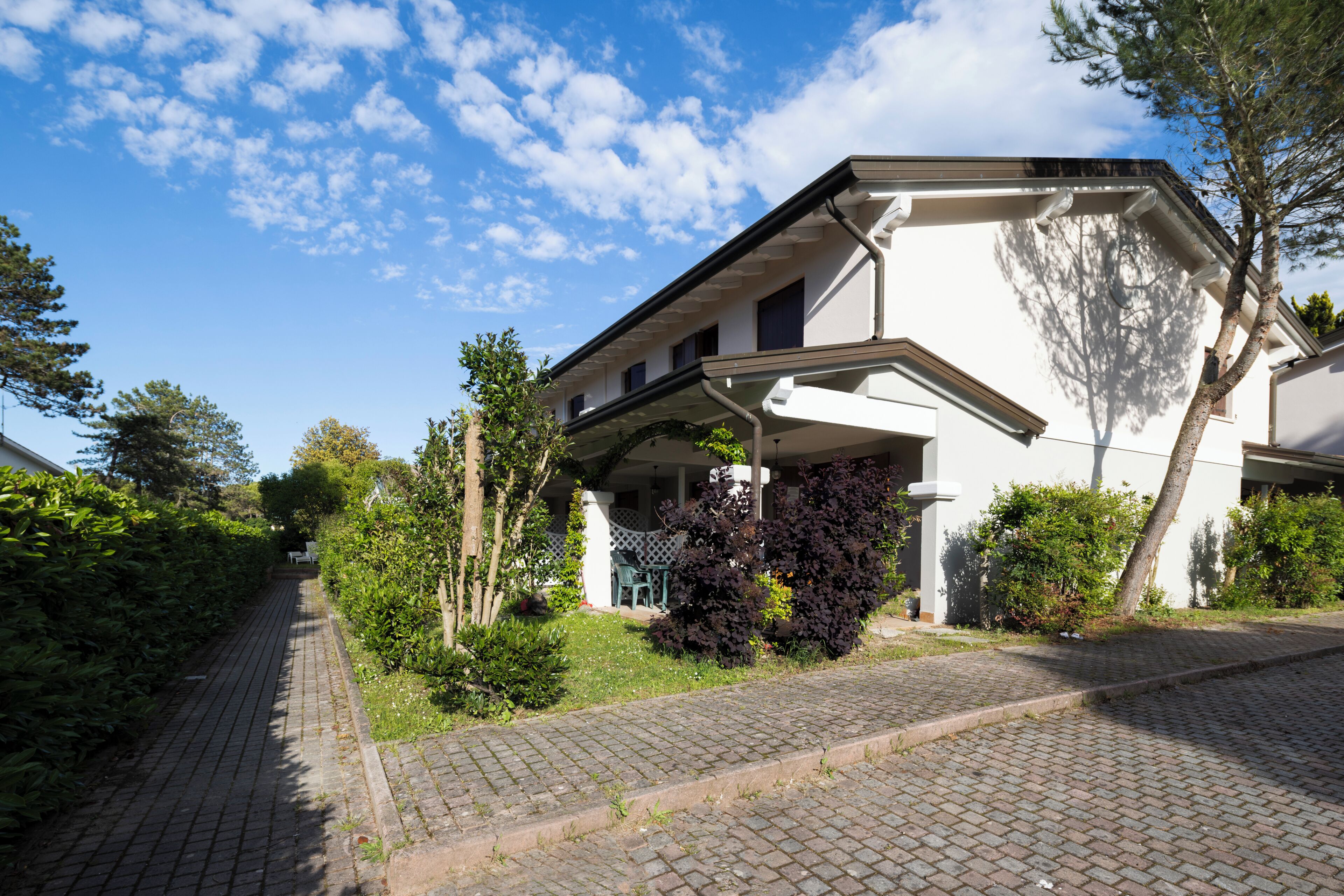 Een huis met twee verdiepingen, een overdekte veranda en een met bakstenen bestraat pad dat naar de ingang leidt.