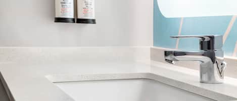 A bathroom with a white sink, a modern faucet, and two bottles of hand soap and lotion on the wall.