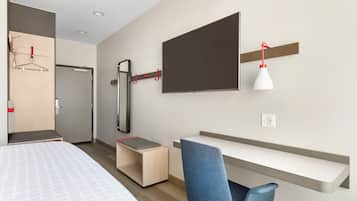 Una habitación de hotel moderna con cama, escritorio, silla, televisor y espejo.