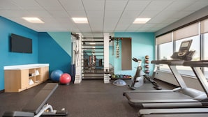 Une salle de sport équipée de tapis de course, de ballons d’exercice et d’un téléviseur fixé au mur.