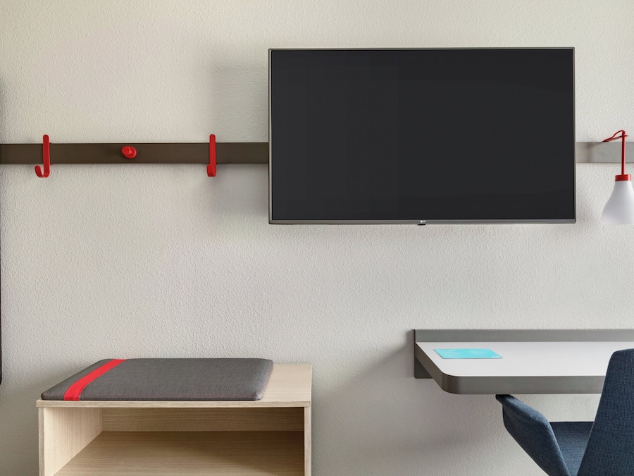 A modern room with a flat-screen TV mounted on the wall, a desk with a chair, and a bench with a red stripe.