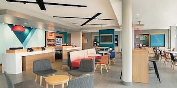 A modern hotel lobby with a reception desk, seating area, and a TV screen.