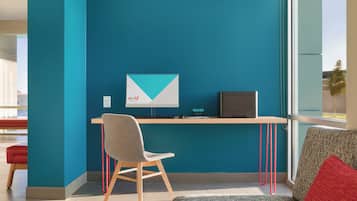 Un moderno spazio ufficio con una parete color petrolio, una scrivania con un computer, una sedia e un divano rosso.