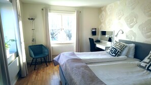 Habitación de hotel con dos camas, un escritorio, una silla, un radiador y una ventana con cortinas.