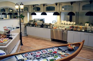 Montaje de bufé con diversos alimentos, y una barca de madera llena de frutas y verduras.