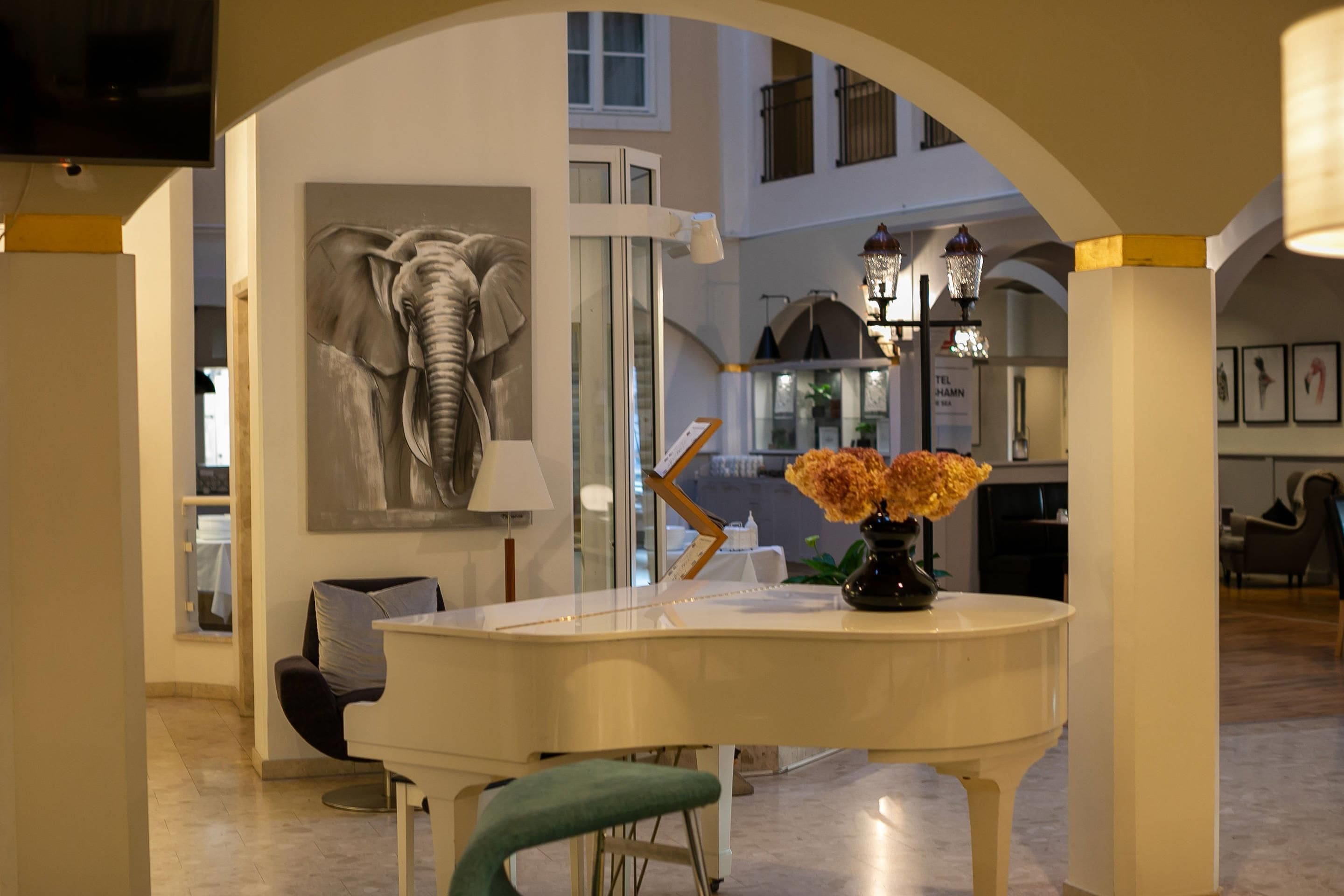 A dining area with a white table, a chair, a vase with flowers, and a large elephant sculpture on the wall.