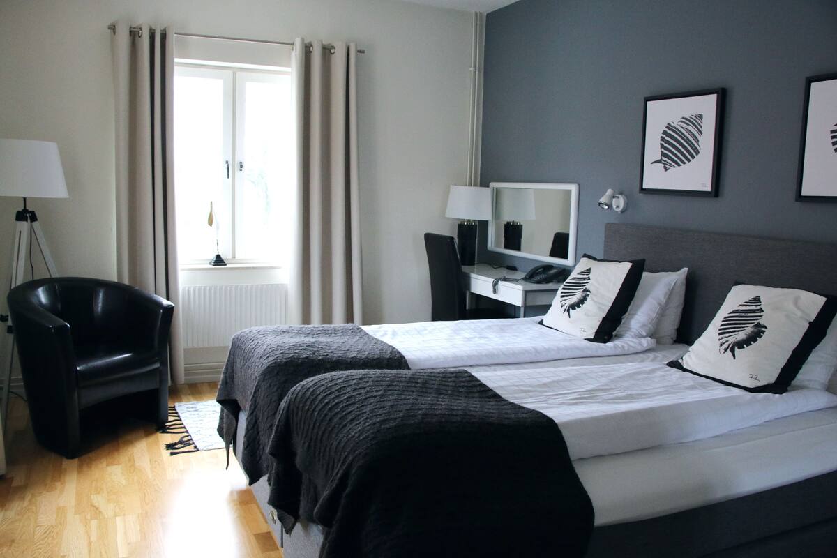 A hotel room with two beds, a desk, a chair, a lamp, and a window with curtains.