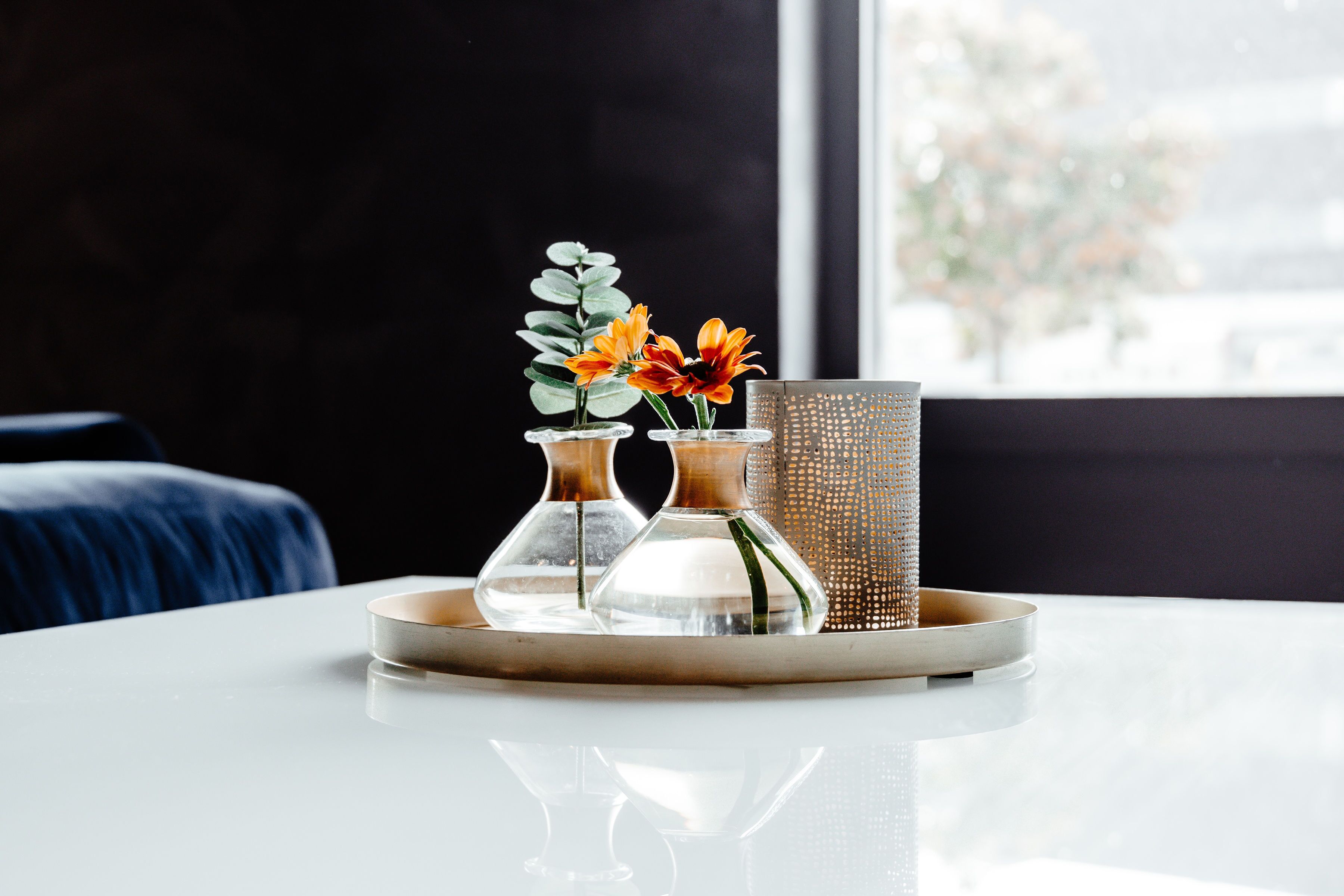 A white table with two clear glass vases containing flowers and a textured metal vase.