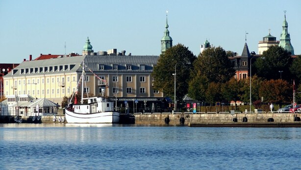 Udsigt over vandet med en historisk bygning, en båd ved kajen og en klar himmel.