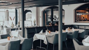 En restaurantindretning med høje borde, grå polstrede bænke og hvide duge.