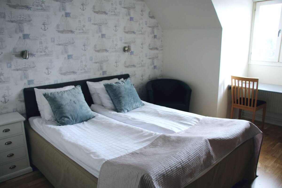 A bedroom with a bed, two pillows, a nightstand, a chair, and a window.