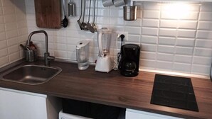 Una cocina con un lavabo, una cafetera, una licuadora y utensilios colgando.