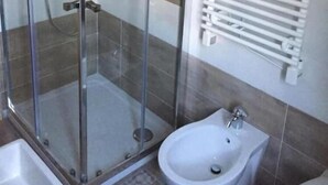 Un baño con ducha de vidrio, un bidé y un radiador fijado a la pared.