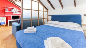 Un dormitorio con una cama grande, un escritorio con ordenador, una estantería y una ventana con vistas.