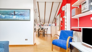 Una sala de estar moderna con un sillón azul, un televisor de pantalla plana y una zona de comedor con una mesa y sillas.