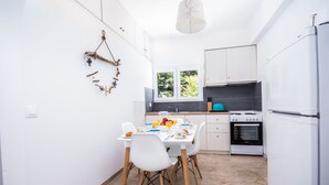 Una cocina compacta con armarios blancos, una mesa de comedor con sillas, una lámpara colgante y una ventana con vistas a zonas verdes.