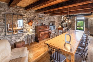 Une cuisine rustique avec des murs en pierre, des poutres en bois, une longue table en bois et un piano.