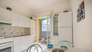 A compact kitchen with white cabinets, a stove, and a dining area with a table and chairs. - La Casa del Mare close to the beach (Nerano)