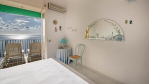 A bedroom with a balcony overlooking the sea, a bed, a chair, a small table with a lamp, and a wall with a mirror and decorations. - La Casa del Mare close to the beach (Nerano)