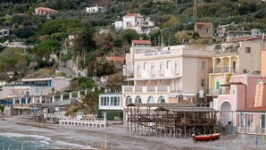 A coastal building named 'Taverna del Capitano' with a beach in the foreground and a rocky hillside in the background. - La Casa del Mare close to the beach (Nerano)