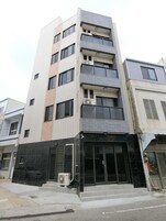 A multi-story building with a modern design, featuring a mix of brick and tiled facades, large windows, and a prominent entrance with a glass door.