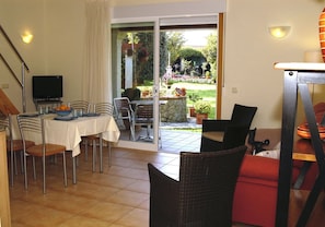 A dining area with a table and chairs, a television, and a view of a garden through a sliding door. - Duplex with 2 bedrooms (4 adults) (O Grove)