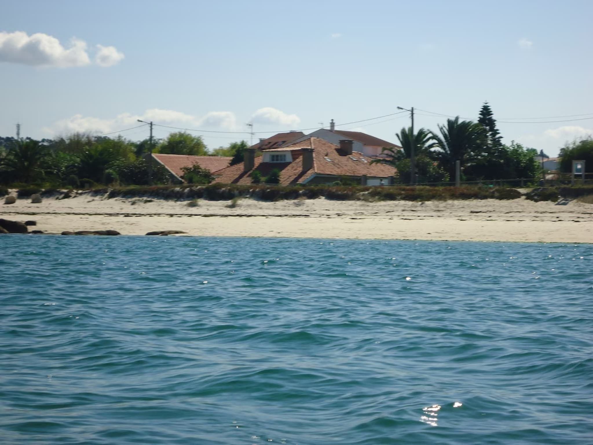 Ein Küstenhaus mit Ziegeldach, gelegen an einem Sandstrand mit Blick aufs Meer.