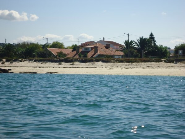 Ein Küstenhaus mit Ziegeldach, gelegen an einem Sandstrand mit Blick aufs Meer.