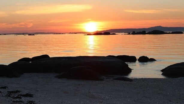 Un atardecer sobre un cuerpo de agua tranquilo con rocas grandes al frente.