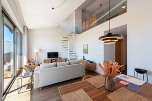 Uma sala de estar moderna com sofá, mesa de jantar e escada que leva a um andar superior.