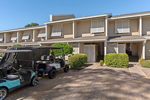 Un hotel de varios pisos con un camino pavimentado, un carrito de golf y arbustos cuidadosamente podados.