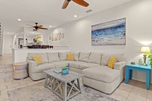 Una sala de estar con un sofá modular, una mesa de centro, un ventilador de techo, un cuadro y una lámpara.