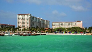 A coastal hotel with multiple high-rise buildings, a pier with boats, and a beach area with umbrellas.