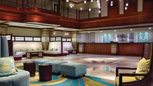 A spacious lobby with a high ceiling, wooden paneling, and a central seating area with sofas and ottomans.