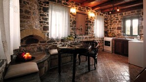 A rustic stone kitchen with a fireplace, wooden table, and stone walls. - Palaeopoli Villas (Kithira)