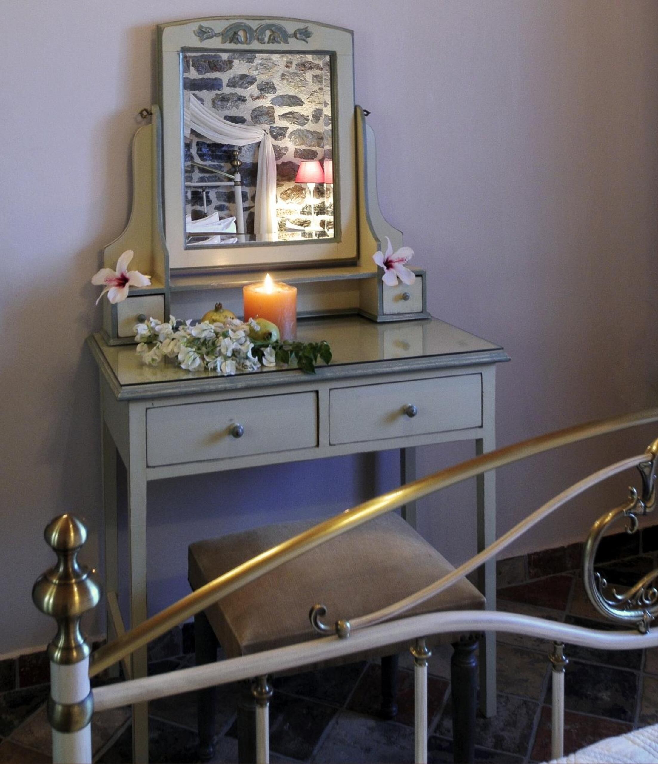 Un tocador de estilo vintage con espejo, una vela encendida y flores decorativas.