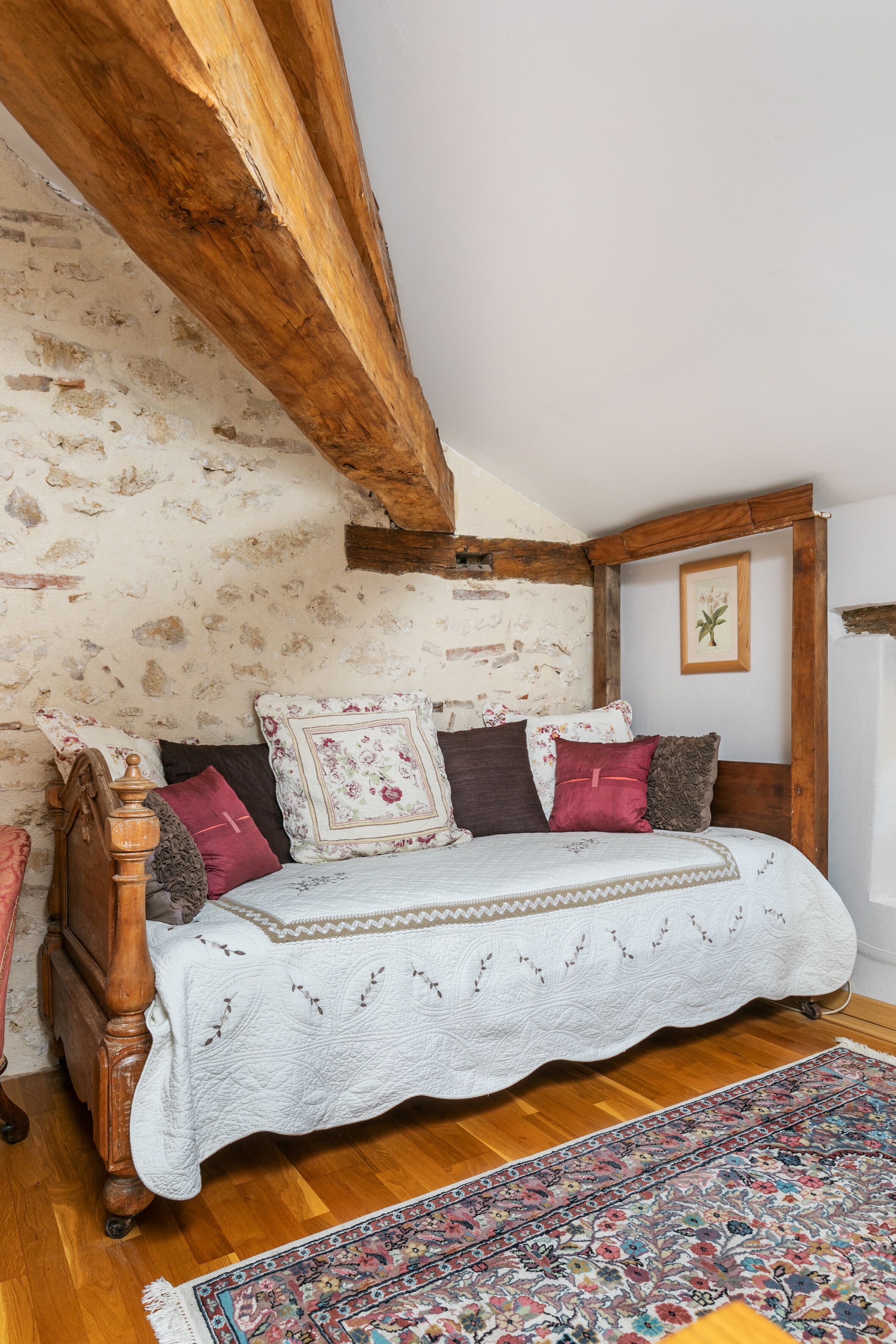 A rustic bedroom with exposed wooden beams, a wooden bed frame, and a patterned rug.