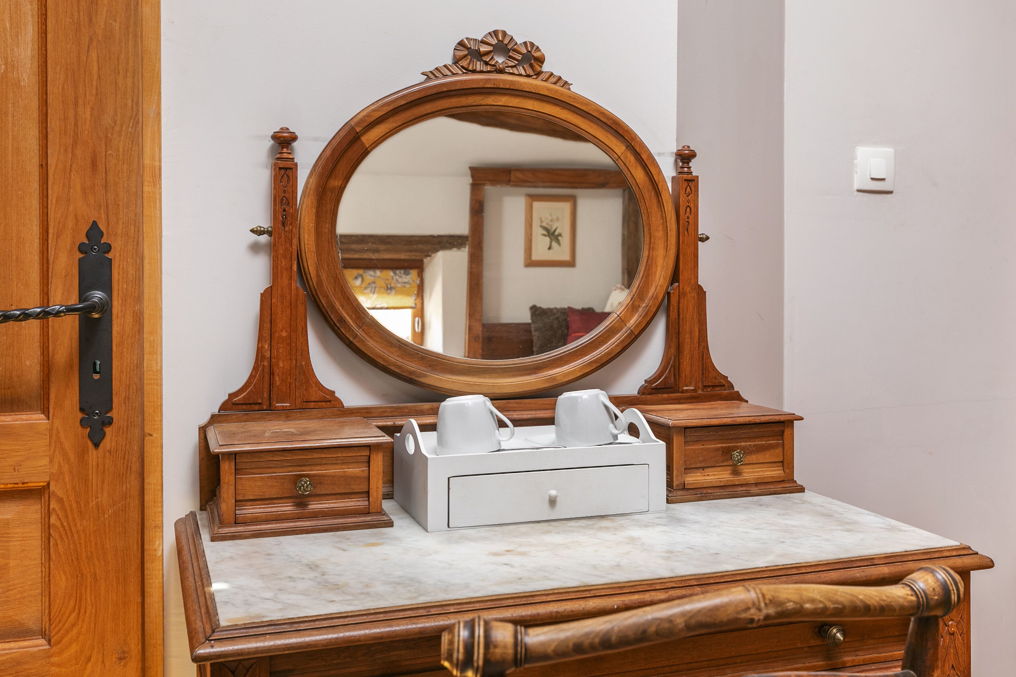 A wooden dresser with a marble top, a mirror, and a tray with cups.