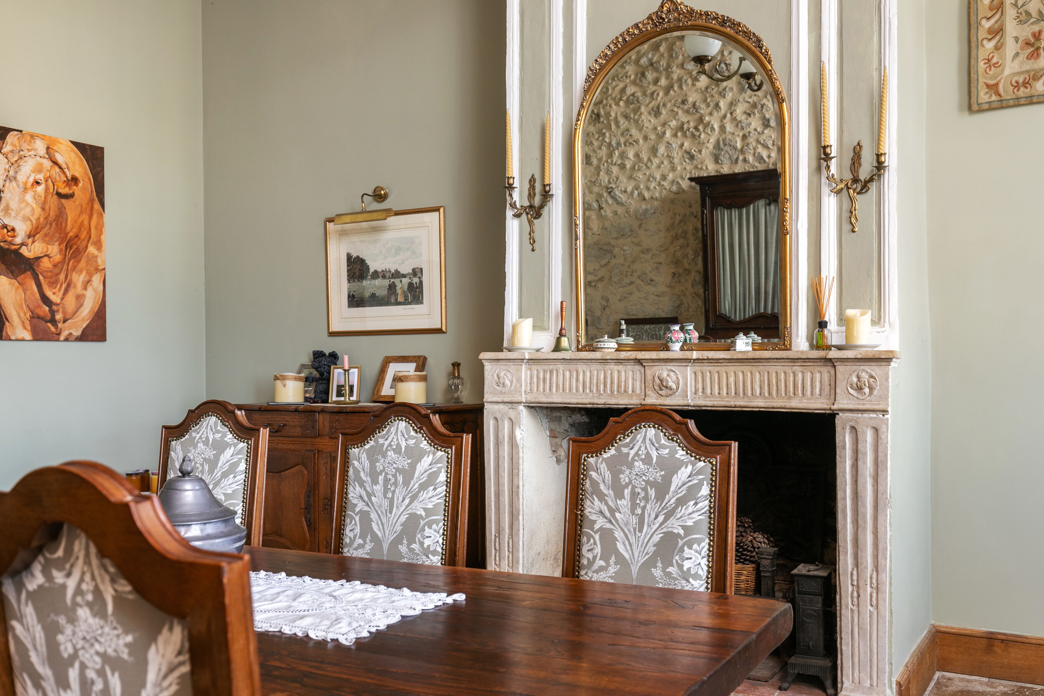 A dining room with a wooden table, ornate chairs, a fireplace, and a large mirror.