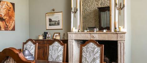 A dining room with a wooden table, ornate chairs, a fireplace, and a large mirror.